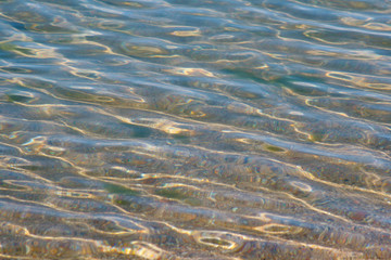 Beautiful background texture with transparent water of Baikal, translucent bottom of the reservoir, sparkling highlights on the waves