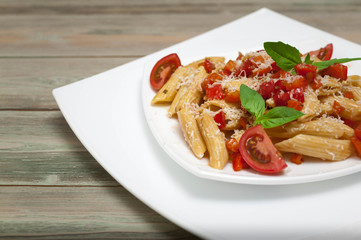 Penne pasta with vegetables and parmesan cheese on a white square plate on a wooden table.