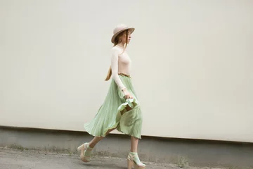 Young red hair girl in hat, dressed in beige blouse and turqoise pleats skirt, on light street backgraund.  Fashion and stylish concept. © Dubrovskyi Oleksii