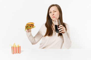 Woman drink cola from straw glass bottle, sitting at table with burger, french fries isolated on white background. Proper nutrition or American classic fast food. Advertising area with copy space.