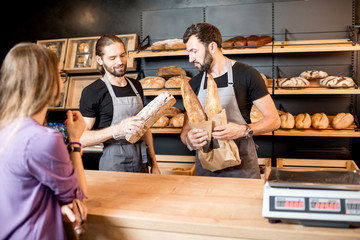 Woman buying bread in the bakery shop with man sellers