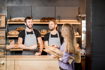 Woman buying bread in the bakery shop with man sellers