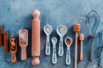 Kitchen utensils for baking, rolling pin and measuring spoons on a blue table with copy space. Cooking pastry concept.