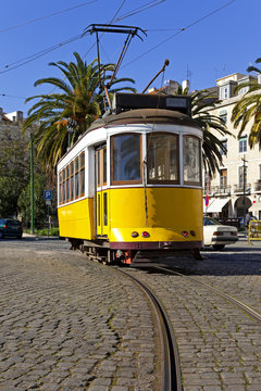 .Iconic 100 year old Lisbon yellow tram in Campo das Cebolas on the Baixa District of Lisbon, Portugal. View of the rails and cobblestone road pavement.