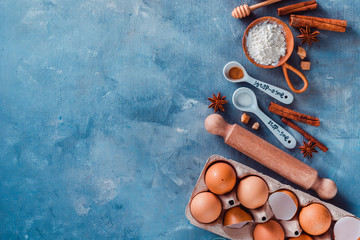 Cooking pastry concept from above. Kitchen utensils for baking, flour, sugar, whisks, cookie cutters and a rolling pin a blue table with copy space.