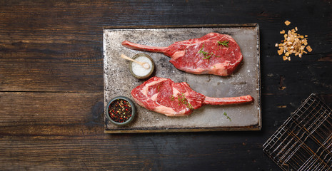 Raw Tomahawk steak on on old metal tray ondark old wooden background with spices for grilling or preparation for smoking, top view, copy space