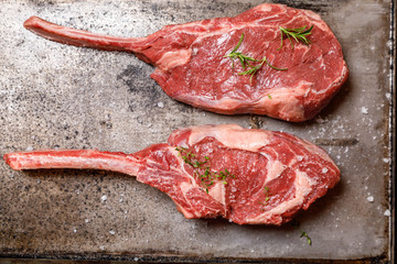 Raw Tomahawk steak on on old metal tray ondark old wooden background with spices for grilling or...