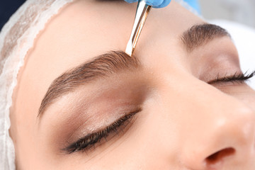 Young woman having professional eyebrow correction procedure in beauty salon