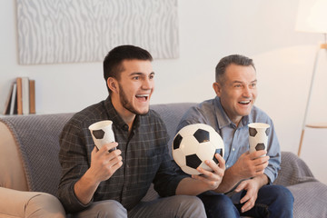 Mature man and his son watching football match on TV at home