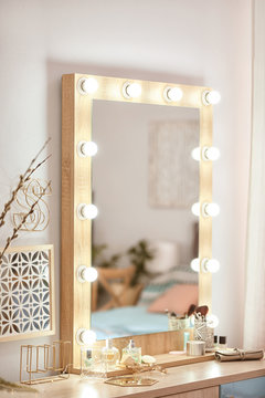 Mirror with light bulbs and cosmetic products on dressing table indoors