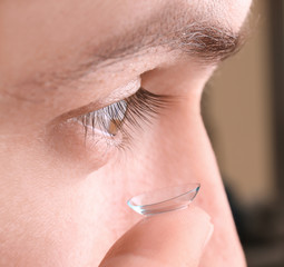 Young man putting contact lens in his eye, closeup