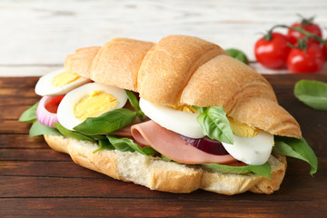 Tasty croissant sandwich with sausage and eggs on wooden board