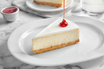 Pouring sweet jam onto delicious cheesecake served on plate