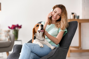 Young woman talking on phone while stroking her dog at home - Powered by Adobe