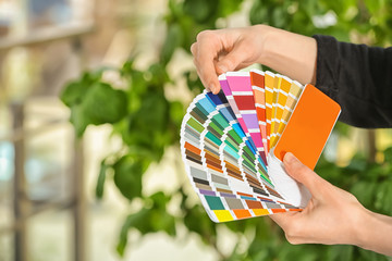Female designer holding color palette samples on blurred background