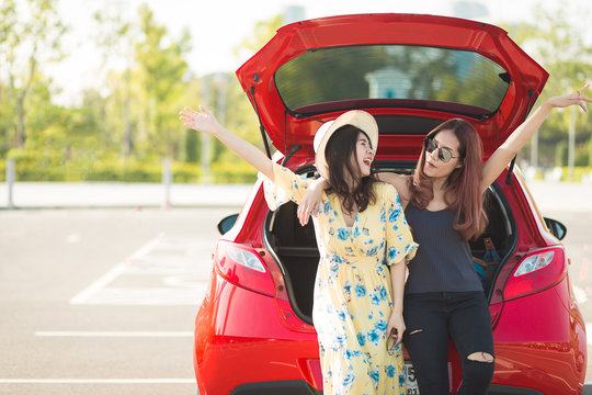Enjoying woman with her girlfriend traveler sitting on hatchback red car. summer vacation, holidays, travel, road trip and people concept .