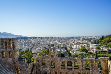 Fototapeta na wymiar View of Athens cityscape through ancient stone theatre seeing lowrise white buildings architecture, mountain, trees and clear blue sky background