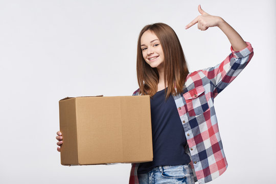 Delivery, relocation and unpacking. Happy young woman holding cardboard box pointing at box with copy space
