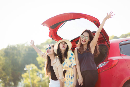 Enjoying woman with her girlfriend traveler sitting on hatchback red car. summer vacation, holidays, travel, road trip and people concept .