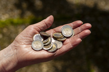 Many Euro coins on the hand of an old woman. 