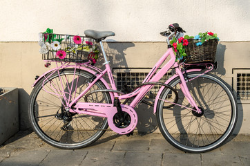 old pink bicycle with flowers in front of a building