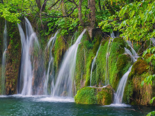 Scenic waterfall deep in the forest with streams of crystal clear water and moss on the stones.