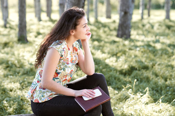 happy young girl sitting on a log in the forest, bright sunlight around, beauty of nature in spring