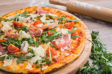 Fresh pizza with prosciutto meat, tomato and green arugula
