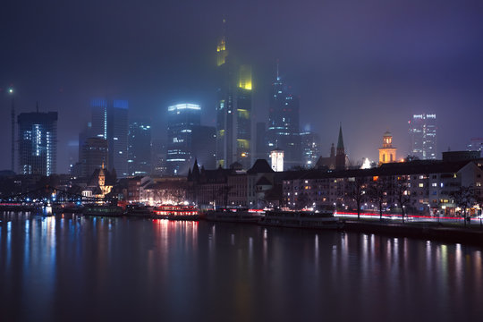 Picturesque view of business district with skyscrapers and Old Town with mirror reflections in the river during foggy morning blue hour, Frankfurt am Main, Germany