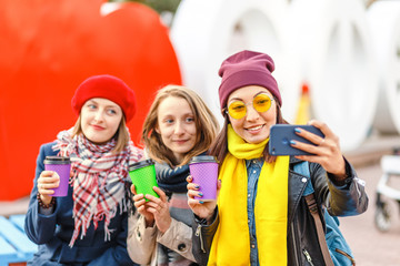 Fototapeta premium happy young women with take away cups outdoors taking selfie with smartphone