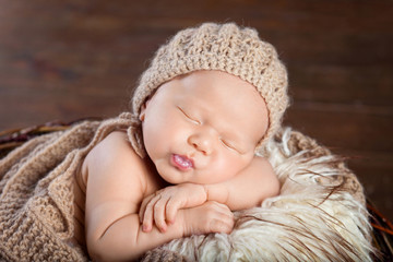 Fototapeta na wymiar Beautiful little newborn boy 20 days sleeps in a basket whith knitted plaid. Portrait of pretty newborn boy