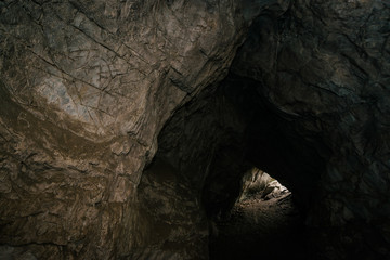 Beautiful cave. View from inside dark dungeon. Textured walls of cave. Background image of underground. Dampness inside cave. Light at end of tunnel.