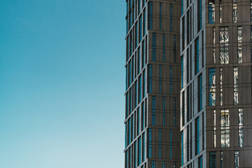 Side view of a modern skyscraper glassy facade with a copy space area for advertising text on the left; fragment of a contemporary high-rise made of concrete and glass with a blue sky empty area