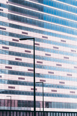 Glass facade of an office skyscraper under construction: plenty of dusty windows of empty offices, tiles, lanterns; color tint to pink, blue sky reflecting in the glass