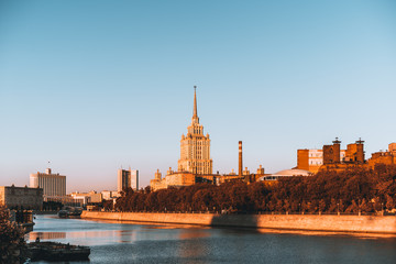 Sunset in Moscow, Russia: government White Hous, high-rise, brick chimney lit by evening sun in the background and water of Moscow-river in the foreground, clear blue sky