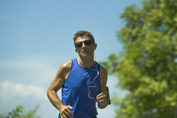 Fototapeta premium young attractive sport runner man training in asphalt road running workout a sunny Summer morning surrounded by trees and vegetation