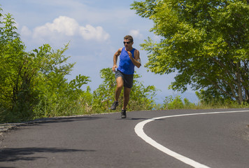 young attractive sport runner man training in asphalt road running workout a sunny Summer morning surrounded by trees and vegetation