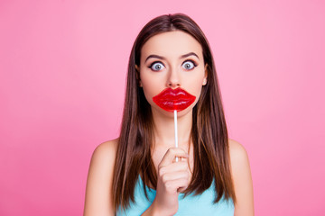 Concept of having lips injection. Portrait of shocked amazed wondered with big round eyes beautiful cute lovely girl holding big bright red lollipop over mouth, isolated on pink background