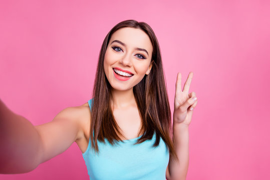 I'm selfie queen! Portrait of cute charming lovely sweet attractive tender girl with straight smooth brown hair taking self picture and presenting v-sign to subscribers, isolated on pink background