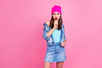 Obraz na płótnie Canvas Attractive cool trendy charming girl wearing denim casual shabby ripped jeans shirt jacket pink hat enjoying the taste of lollipop, isolated on pink background, copy-space