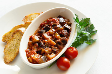 vegan appetizer of eggplant, tomatoes, onion, and garlic on a plate with fried bread, tomatoes, and parsley  