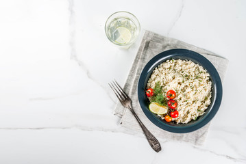 Light dietary food, couscous with tomatoes, lime and fresh herbs in dark bowl, white marble background