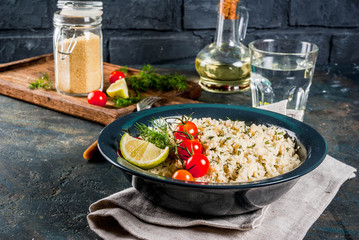 Light dietary food, couscous with tomatoes, lime and fresh herbs in dark bowl, dark blue background copy space