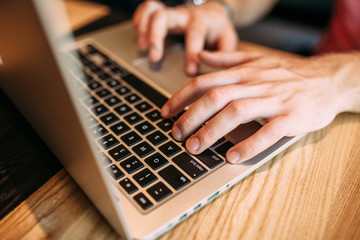 Hands close up of fingers typing on laptop, a man in a cafe