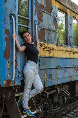 Fototapeta na wymiar A young beautiful girl is standing on the step of an old railway carriage, a departing train