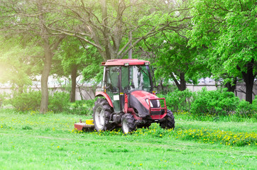 Red tractor and lawn mower, shears lawns in the alleys in the park.