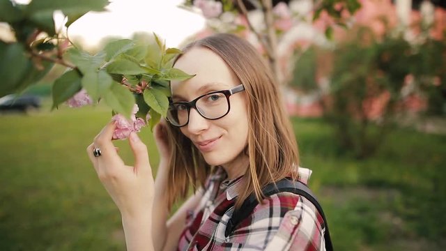 Beautiful girl in glasses posing for a photo. Flowering pink trees in the background. Selective focus.