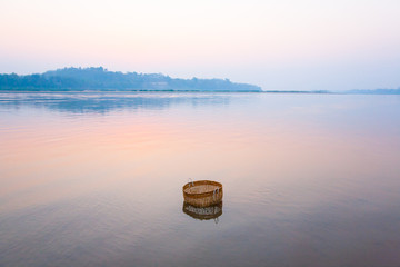 A bamboo basket is dips in mekong river at sunrise.