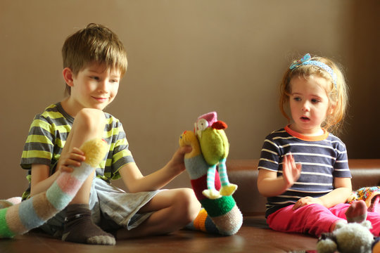 Candid portrait of children playing at home with knitted toys. Emotional facial expressions