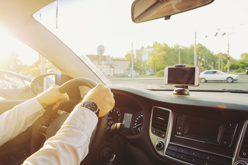 Blank screen cell phone in phone holder mount on dashboard dash panel surface, expensive vehicle interior. Gps navigation concept. Young man hands on steering wheel. Sunset filter background, close up
